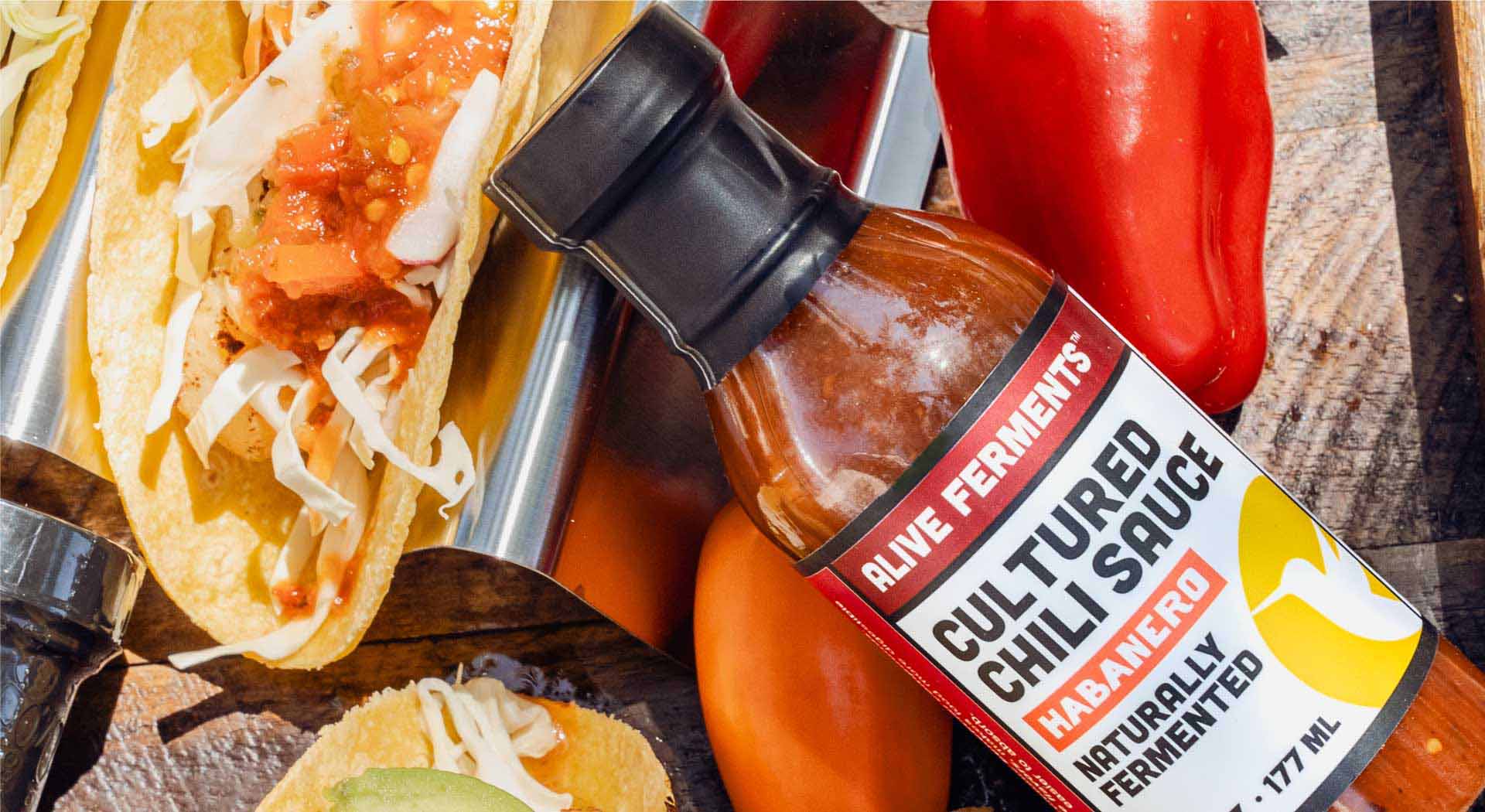 A bottle of fermented habanero sauce sits among a platter of delicious tacos, topped with various probiotic sauces and fresh ingredients.